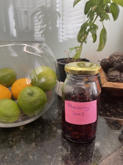 Homemade blueberry jam in a jar next to a bowl of fruit