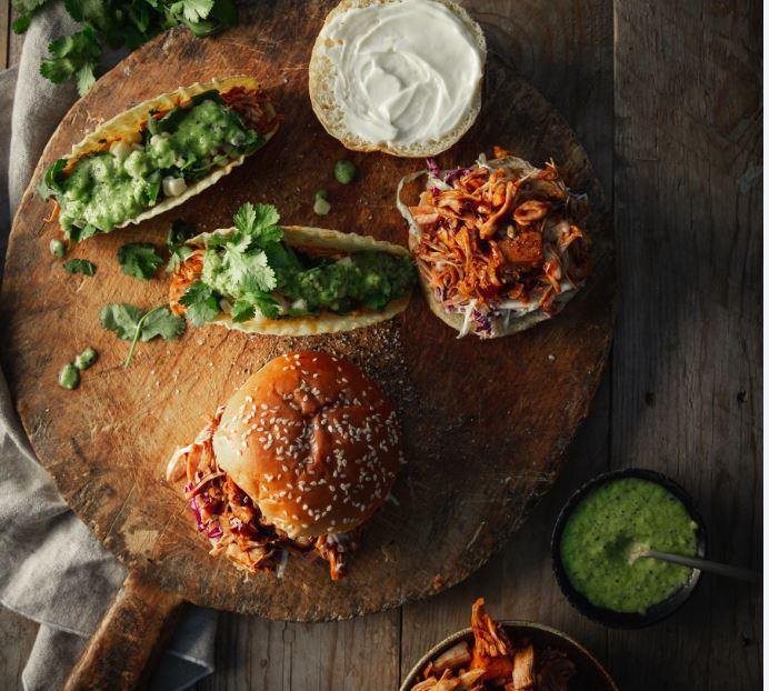 Image of two jack fruit burgers and tacos on a wooden breadboard