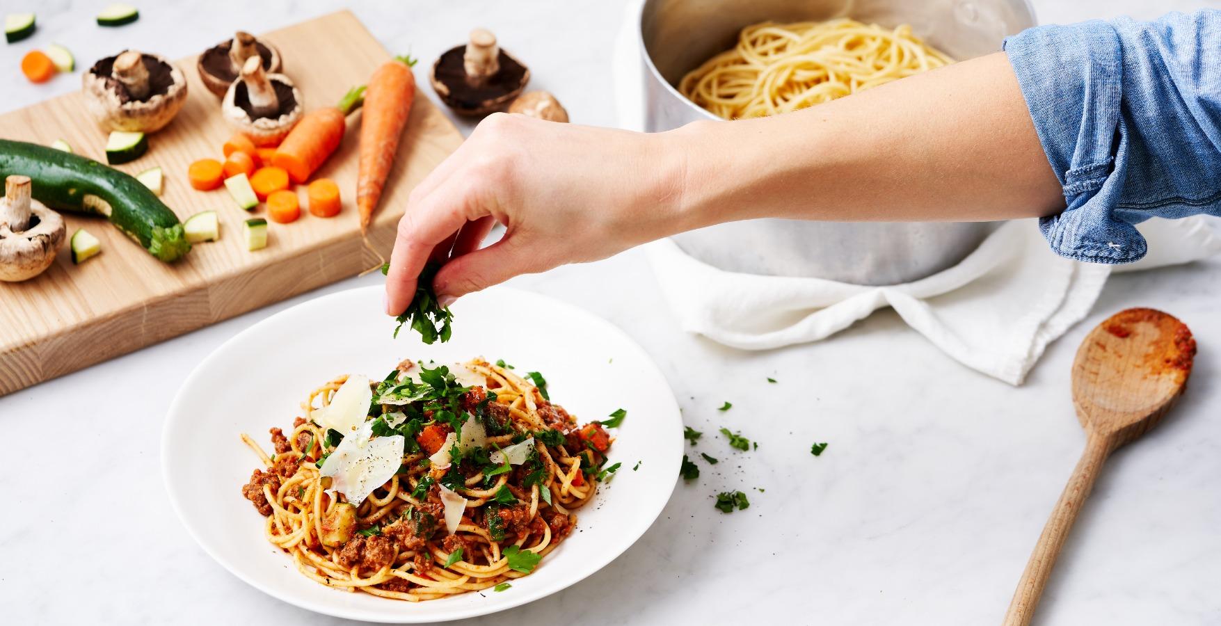 Hand sprinkle herbs over pasta dish