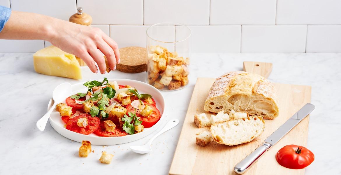 Hand sprinkles herbs over fresh tomato salad