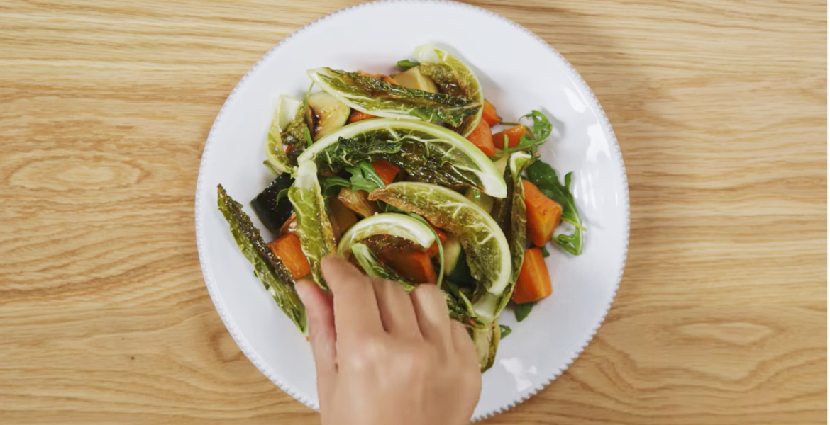 Hand placing roasted cauliflower in salad bowl