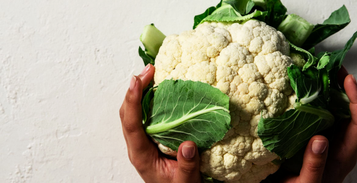 Two hands holding a whole cauliflower