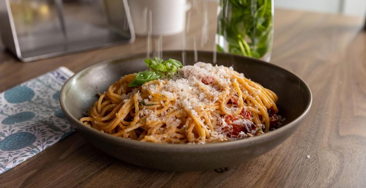 bowl of spaghetti with parmesan being sprinkled on top