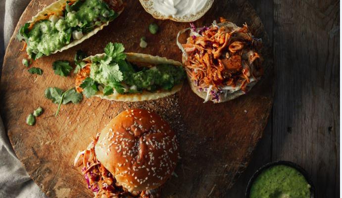 Image of two jack fruit burgers and tacos on a wooden breadboard